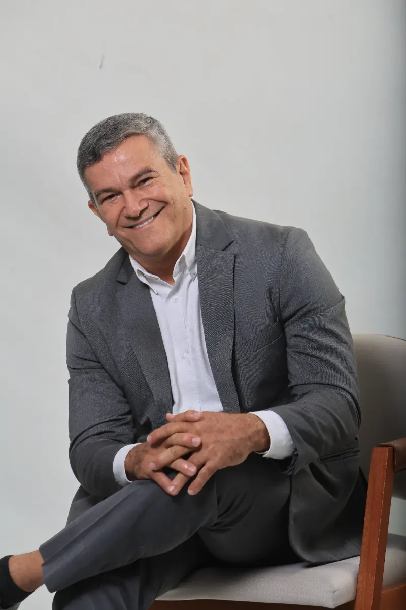 Flávio Cesário sentado, sorrindo, em um retrato de estúdio